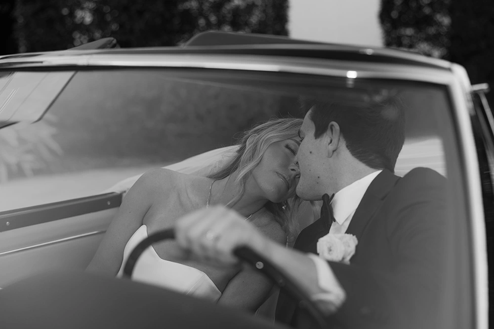 Bride and groom sharing a kiss inside a classic vintage automobile