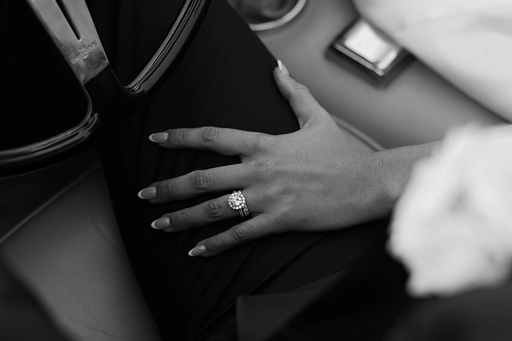 Close-up of bride's diamond ring resting on groom's hand in vintage car