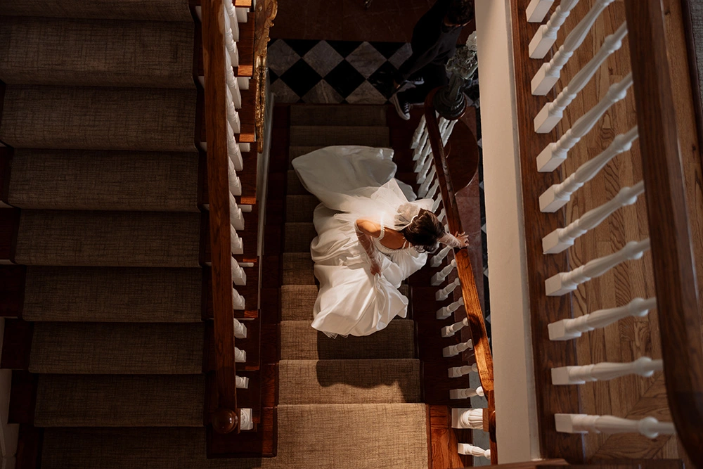 Aerial view of bride in wedding dress descending grand wooden staircase